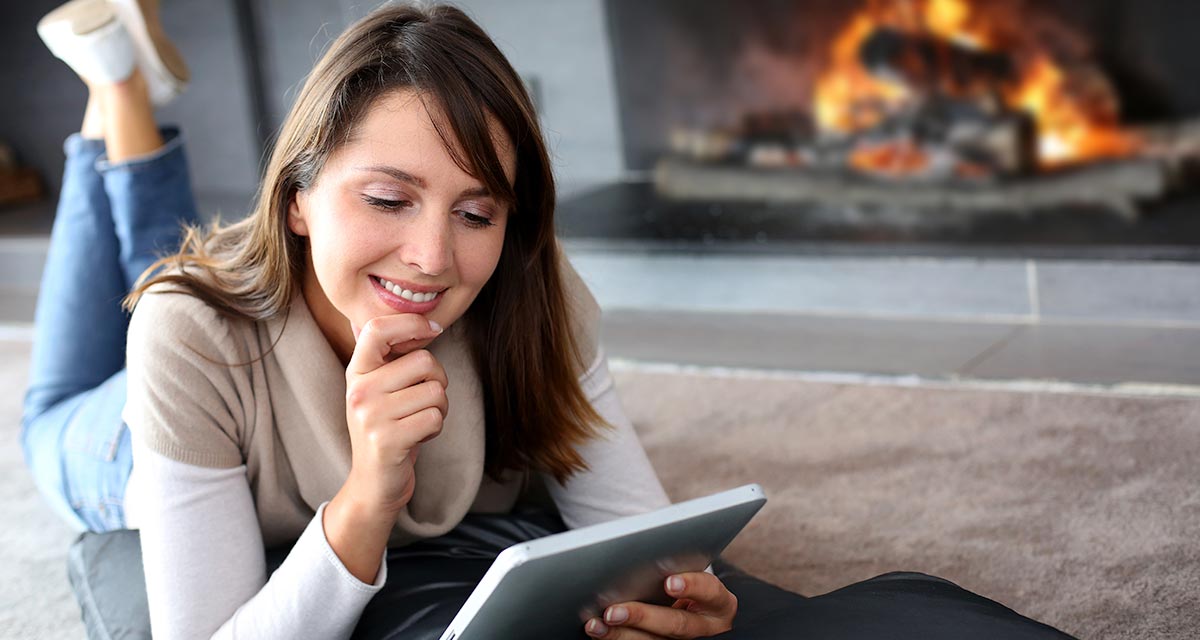 Woman lying on floor looking at tablet in front of fireplace