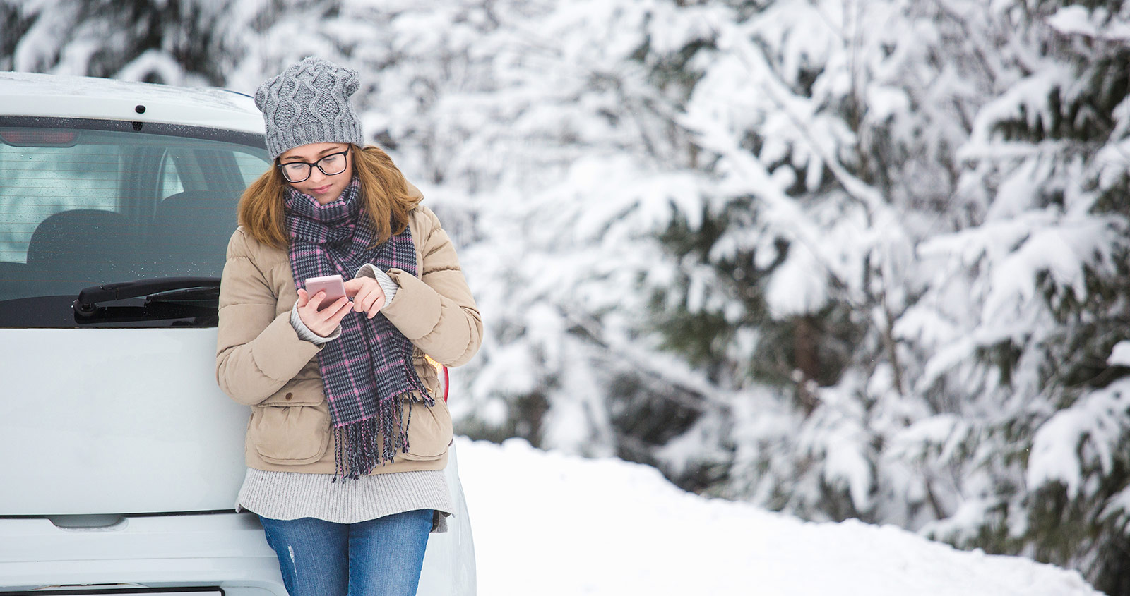 Young woman standing next to car using her smartphone in the winter