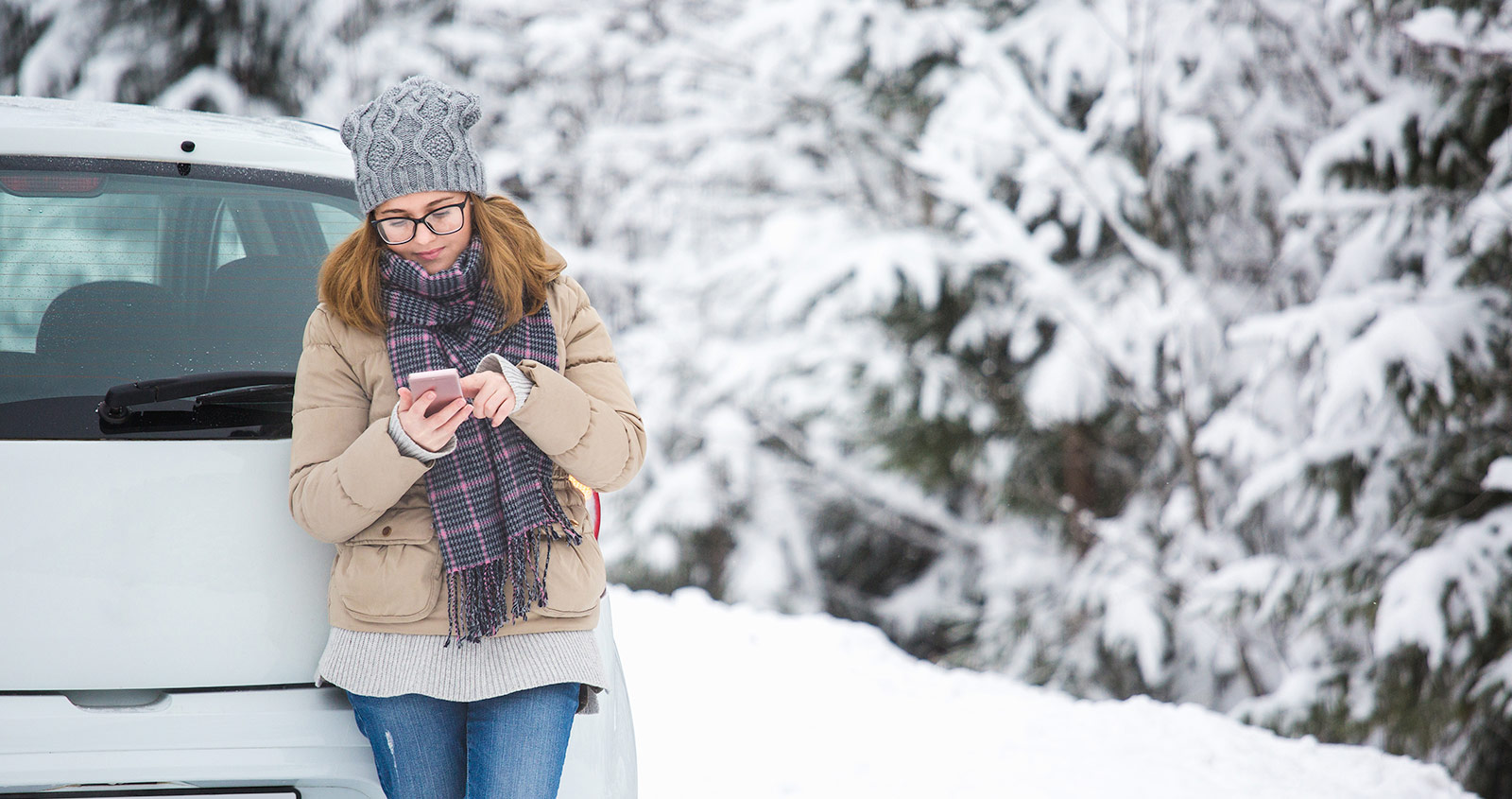 Minimize guest touch points while streamlining processes Young woman standing next to car using her smartphone in the winter