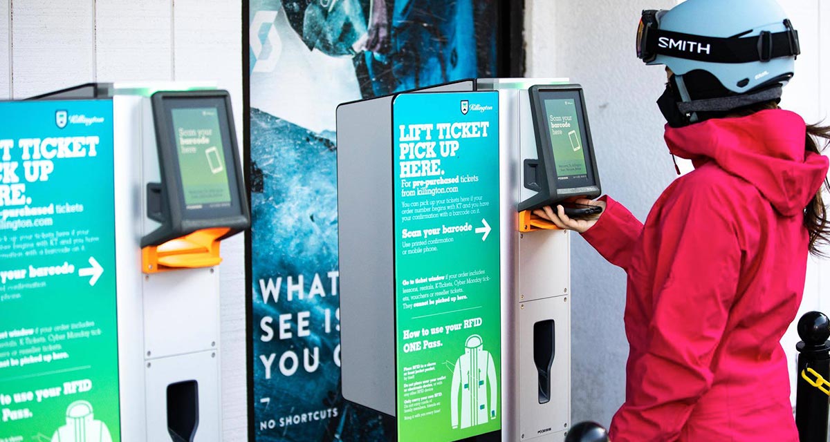 Woman at ski resort at a self-serve lift ticket kiosk wearing a red jacket