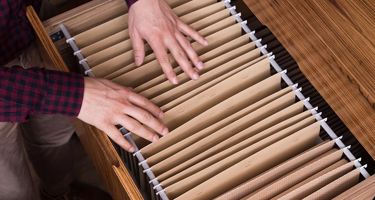 Man in plaid shirt looking at hanging files in a drawer