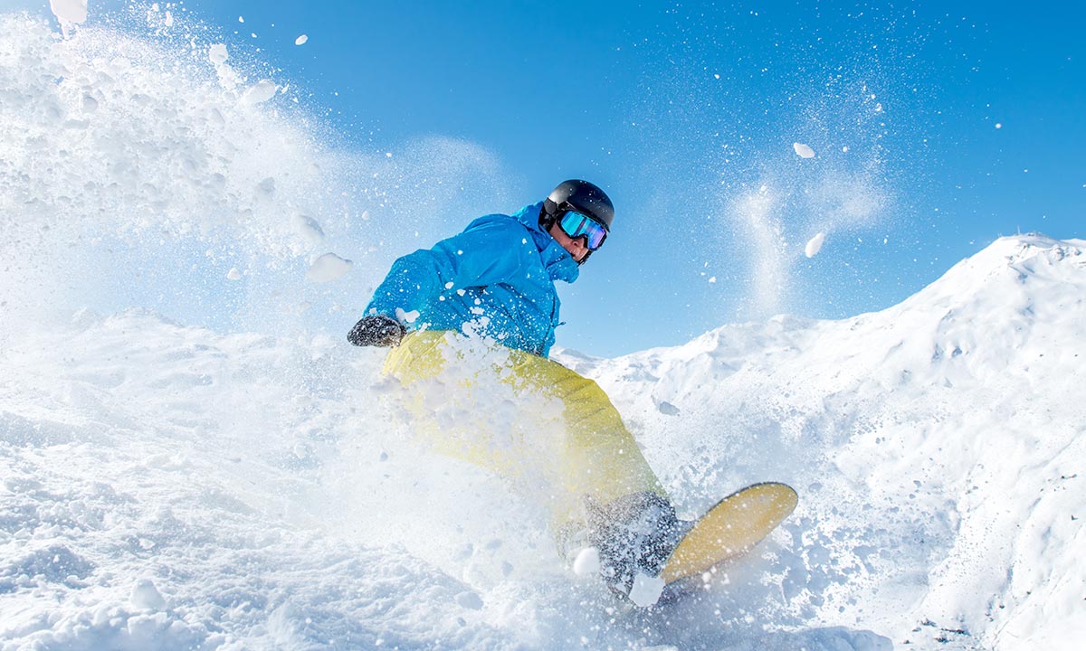 Snowboarding in blue jacket going down a hill